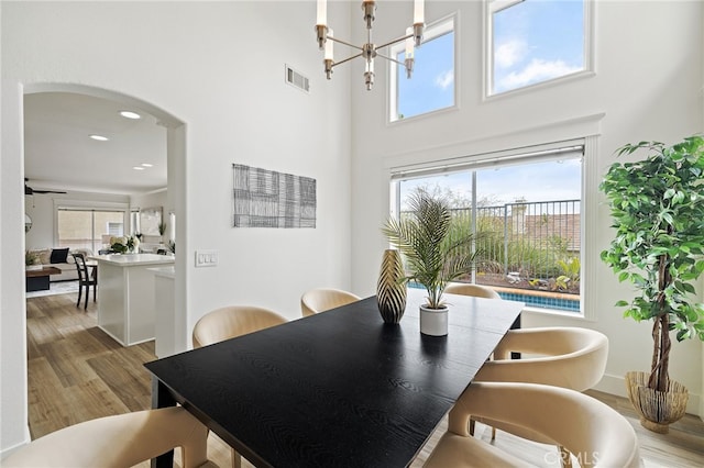 dining room featuring an inviting chandelier, visible vents, a towering ceiling, arched walkways, and wood finished floors