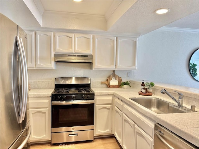 kitchen featuring appliances with stainless steel finishes, under cabinet range hood, a sink, white cabinets, and ornamental molding