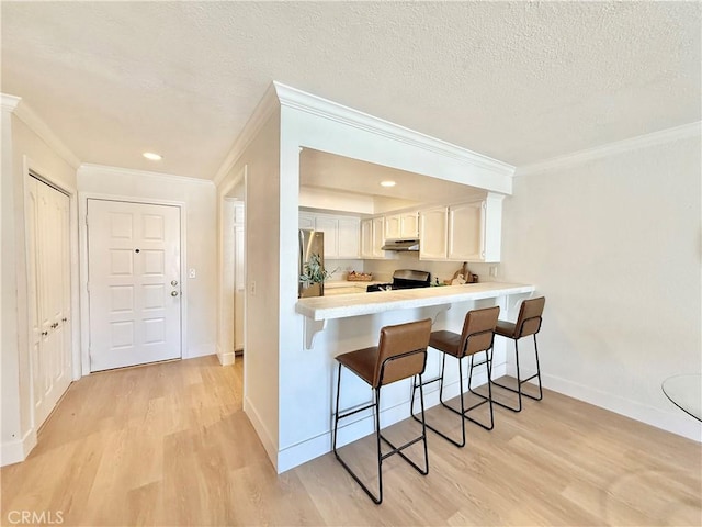 kitchen with under cabinet range hood, appliances with stainless steel finishes, a kitchen breakfast bar, light wood-style floors, and crown molding