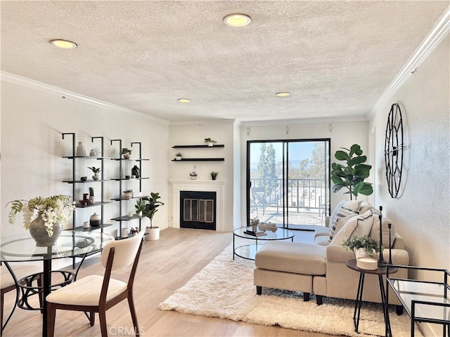 living area featuring light wood-style floors, a textured ceiling, a glass covered fireplace, ornamental molding, and recessed lighting