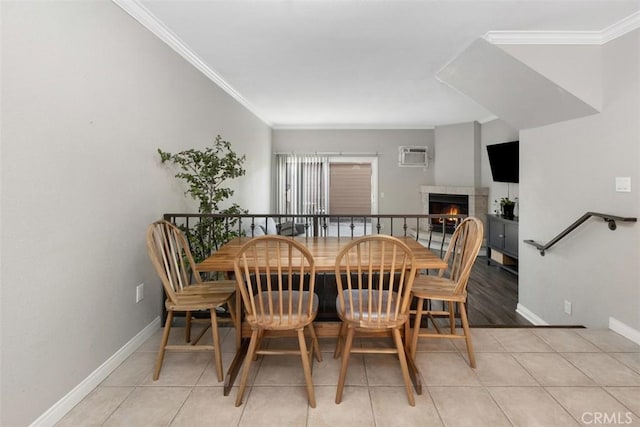 dining space featuring a wall mounted air conditioner, crown molding, light tile patterned floors, a lit fireplace, and baseboards