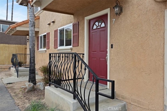 doorway to property featuring fence and stucco siding