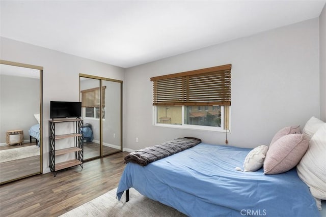 bedroom with two closets, baseboards, and wood finished floors
