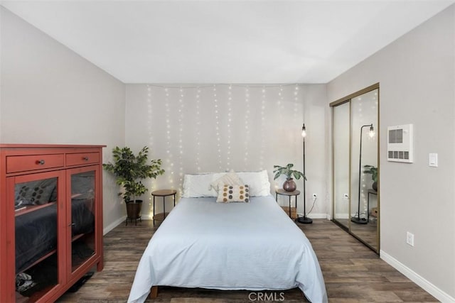 bedroom featuring baseboards, dark wood-style flooring, heating unit, and a closet