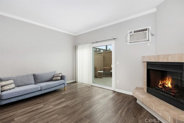 living area with wood finished floors, a tiled fireplace, baseboards, ornamental molding, and a wall unit AC