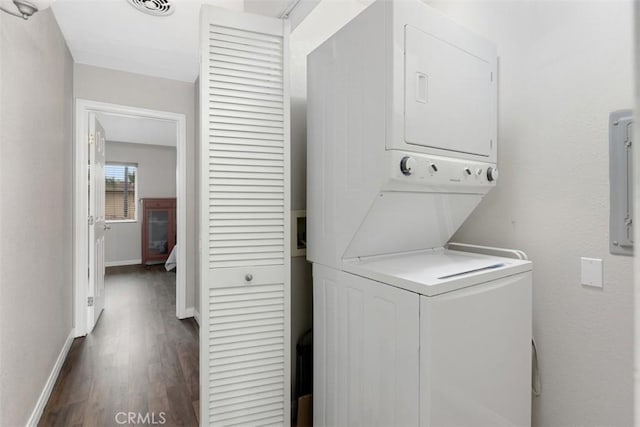 laundry area featuring dark wood-type flooring, stacked washing maching and dryer, baseboards, and laundry area
