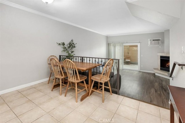 dining space with a wall mounted air conditioner, a warm lit fireplace, light wood-style floors, baseboards, and ornamental molding