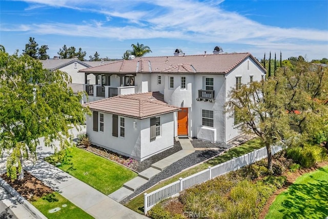 mediterranean / spanish house featuring a tile roof, fence private yard, a balcony, a front lawn, and stucco siding