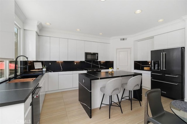 kitchen featuring dark countertops, a sink, a kitchen bar, backsplash, and black appliances