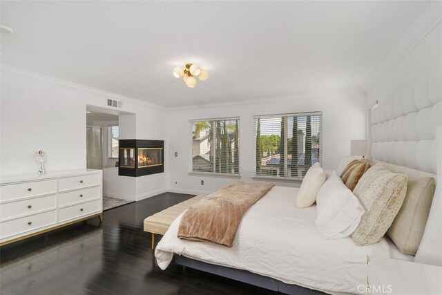 bedroom with crown molding, a multi sided fireplace, wood finished floors, and visible vents