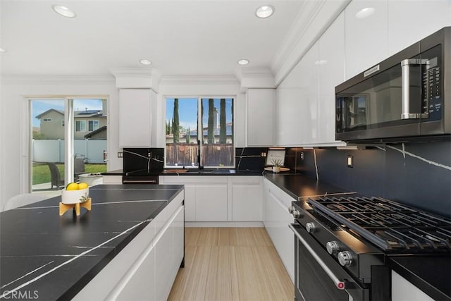 kitchen with dark countertops, decorative backsplash, stainless steel range with gas cooktop, and white cabinetry