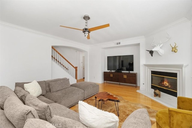 living area with crown molding, ceiling fan, arched walkways, wood finished floors, and visible vents