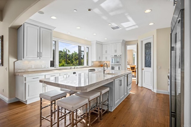 1072 Wiegand, Encinitas, CA 92024 - kitchen with stainless steel appliances, decorative backsplash, hardwood / wood-style flooring, white cabinetry, and an island with sink
