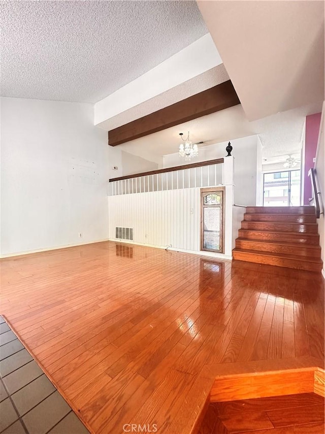 7 Wilderness Pl, Pomona, CA 91766 - unfurnished living room with wood-type flooring, a chandelier, stairs, beamed ceiling, and a textured ceiling