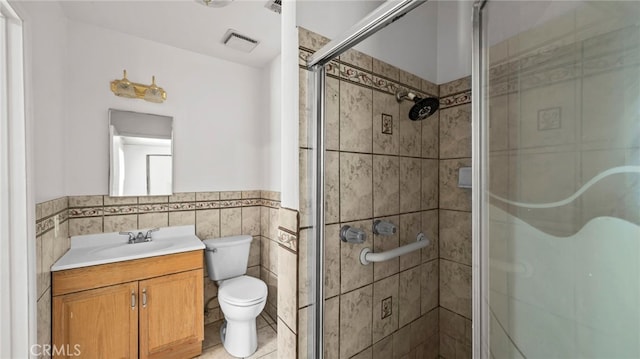 bathroom with tile walls, toilet, a stall shower, vanity, and wainscoting