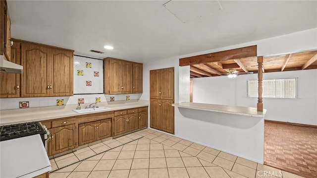 kitchen featuring a sink, brown cabinetry, under cabinet range hood, light countertops, and a peninsula