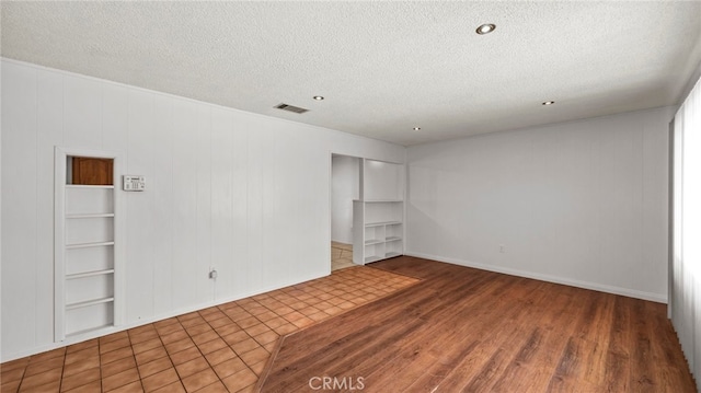unfurnished room with a textured ceiling, wood finished floors, recessed lighting, and built in features