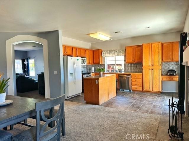 1380 Riverstone Ct, Hemet, CA 92545 - kitchen featuring a center island, arched walkways, decorative backsplash, brown cabinets, and appliances with stainless steel finishes