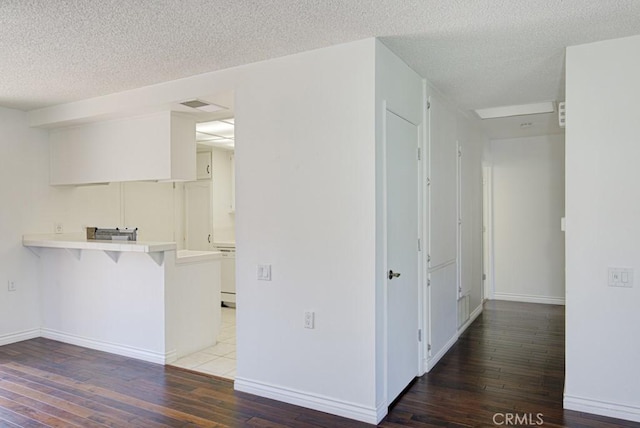 interior space featuring a peninsula, light countertops, a textured ceiling, hardwood / wood-style flooring, and a breakfast bar