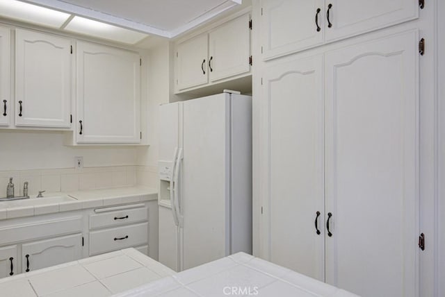 kitchen with white cabinetry, tile counters, a sink, and white refrigerator with ice dispenser