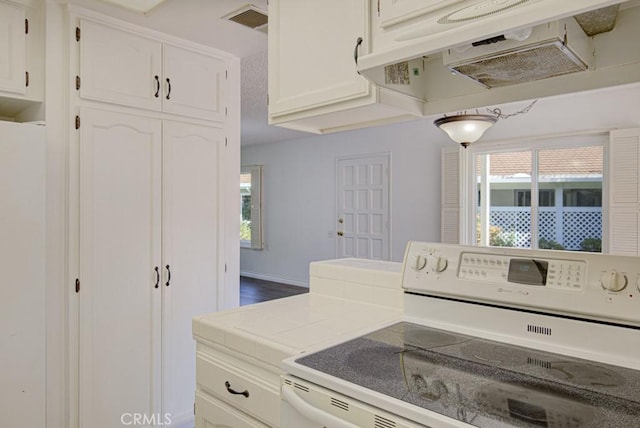 kitchen with electric stove, a wealth of natural light, white cabinets, under cabinet range hood, and visible vents