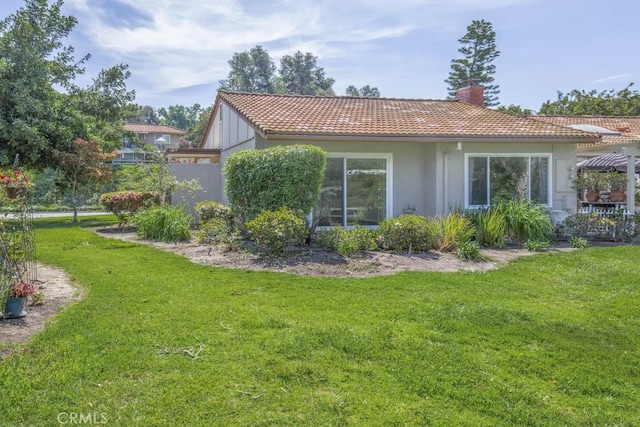 rear view of property with stucco siding, a chimney, a yard, and a tiled roof