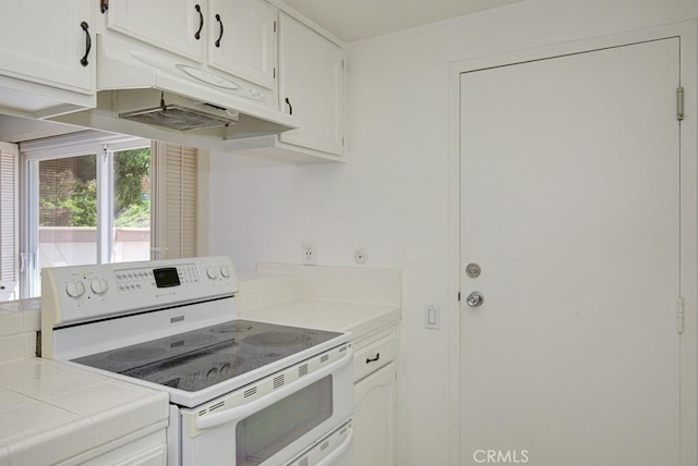 kitchen featuring under cabinet range hood, electric stove, tile countertops, and white cabinetry