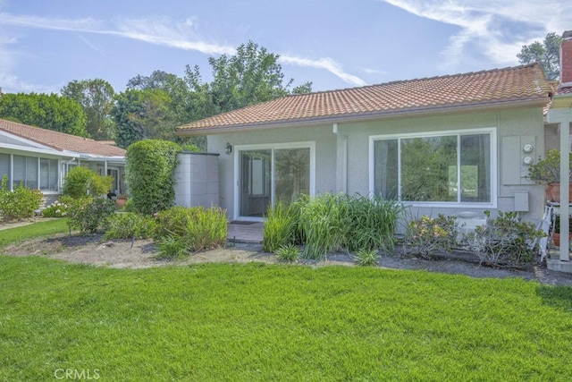 back of property featuring a lawn, a chimney, a tiled roof, and stucco siding