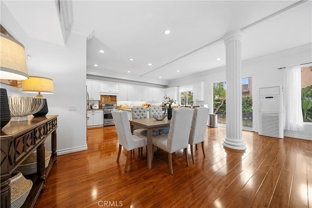 dining area with decorative columns, wood finished floors, and crown molding