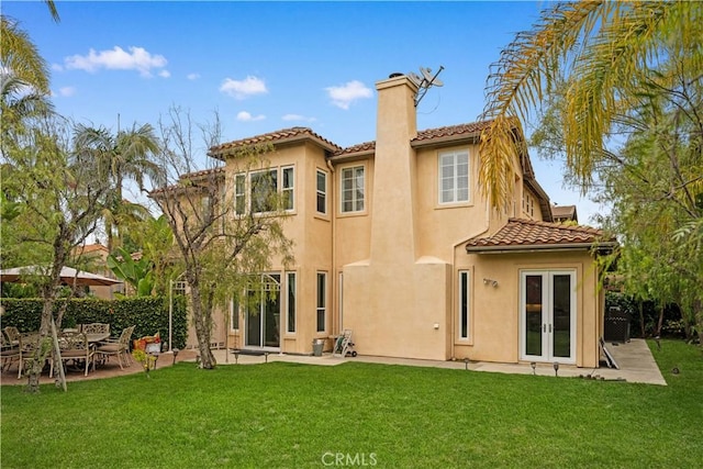 back of property with a tile roof, a chimney, french doors, and stucco siding