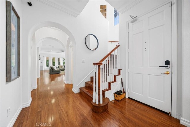 foyer featuring stairway, wood finished floors, arched walkways, baseboards, and ornamental molding