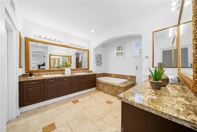 bathroom with a garden tub, stone tile flooring, and vanity