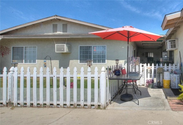 bungalow-style house with stucco siding, an AC wall unit, a patio, and fence