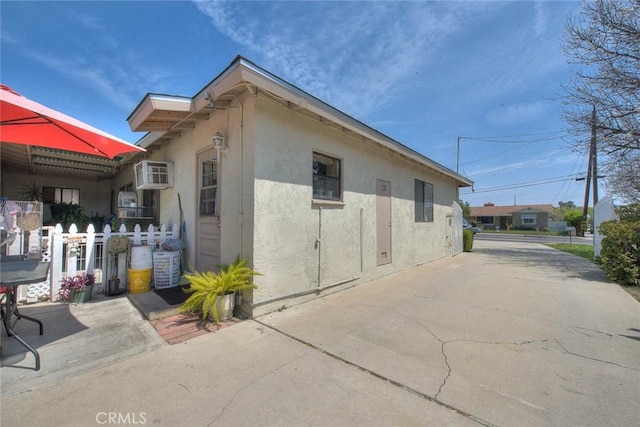 view of side of property with a patio, stucco siding, and a wall unit AC
