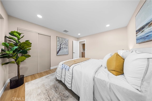 bedroom featuring baseboards, wood finished floors, visible vents, and a closet