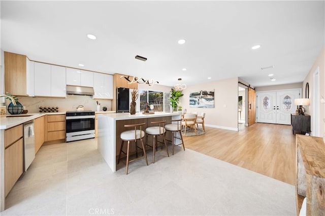 kitchen featuring modern cabinets, electric range oven, dishwasher, under cabinet range hood, and a breakfast bar