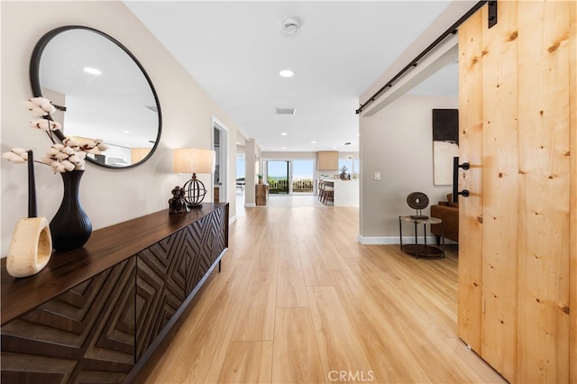 hall with a barn door, recessed lighting, visible vents, light wood-type flooring, and baseboards