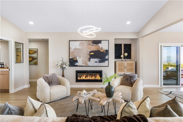 living area featuring a chandelier, a glass covered fireplace, light wood-type flooring, and baseboards