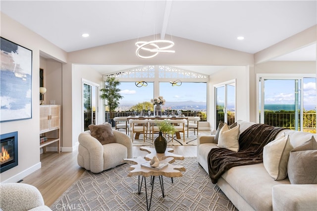 living area featuring wood finished floors, lofted ceiling with beams, a glass covered fireplace, an inviting chandelier, and baseboards