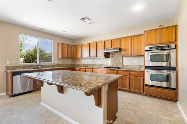 27674 Blue Topaz Dr, Menifee, CA 92585 - kitchen with under cabinet range hood, brown cabinetry, appliances with stainless steel finishes, and visible vents