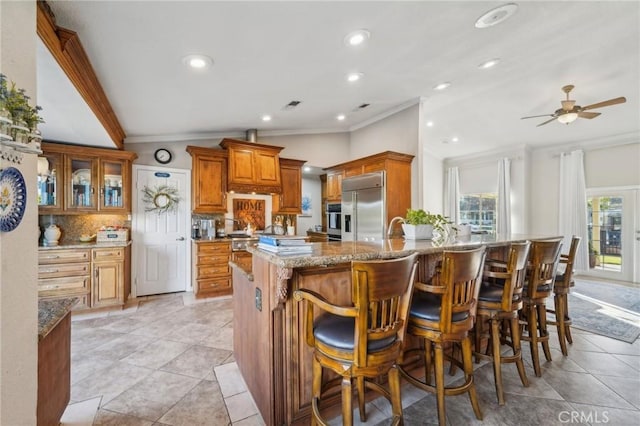 kitchen featuring tasteful backsplash, brown cabinets, light stone counters, crown molding, and appliances with stainless steel finishes