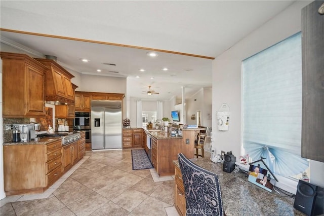 kitchen with tasteful backsplash, dark stone countertops, brown cabinets, stainless steel appliances, and a peninsula