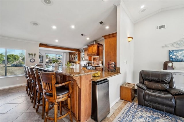 kitchen featuring brown cabinets, vaulted ceiling, visible vents, ornamental molding, and freestanding refrigerator