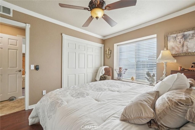 bedroom with wood finished floors, visible vents, a ceiling fan, a closet, and crown molding