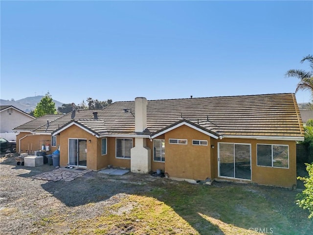 rear view of house with stucco siding, a tile roof, a mountain view, and a lawn