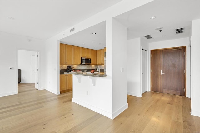 700 W Harbor Dr Unit 402, San Diego, CA 92101 - kitchen with stainless steel microwave, a breakfast bar area, light wood-style flooring, tasteful backsplash, and baseboards