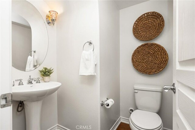 half bathroom with toilet, a sink, and baseboards