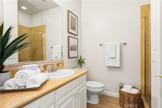 bathroom featuring wood finished floors, toilet, vanity, baseboards, and a stall shower