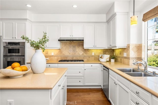 kitchen featuring white cabinets, under cabinet range hood, a sink, appliances with stainless steel finishes, and dark wood-style flooring