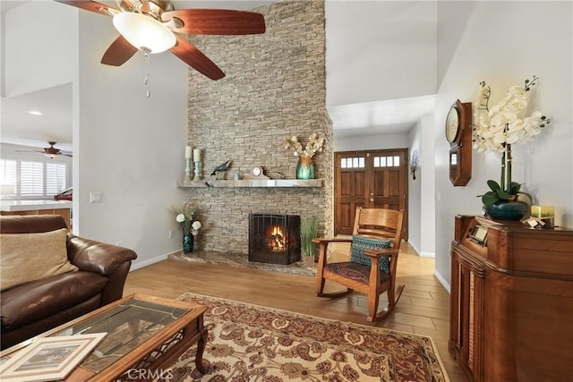 living room featuring a stone fireplace, a towering ceiling, ceiling fan, and wood finished floors